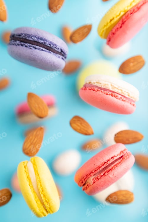 Preview: Multicolored flying macaroons and almonds eggs frozen in the air on blurred blue