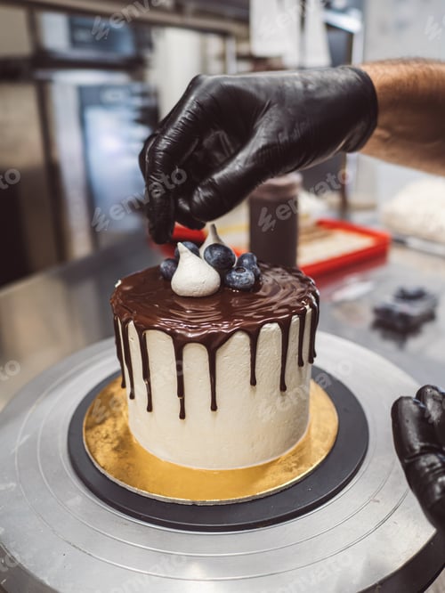 Preview: cake designer decorating a chocolate drip cake with meringue and blueberries