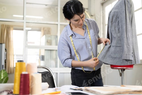 Preview: Closeup young woman tailor taking measurements of jacket on mannequin.