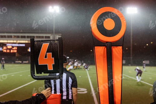 Preview: American football fourth down marker behind referee on rainy game day sideline on the field