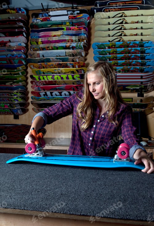 Preview: Teenage girl adjusting skateboard in store