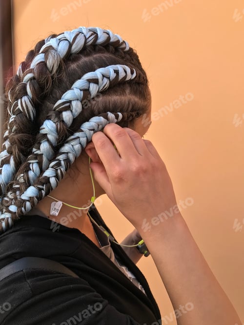 Preview: Girl with blue braids using green wireless headphones / earbuds / earphones. Looking away.