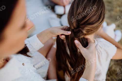 Preview: Close-up of mother making hairstyle to her daughter during family picnic in nature.