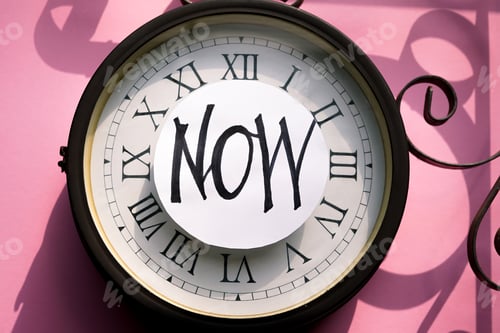 Preview: When the time is right. Flat lay traditional clock on the pink background with the words 'Now'.