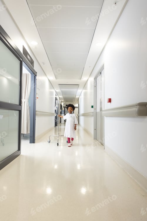 Preview: Happy african american girl patient holding drip and walking in corridor at hospital