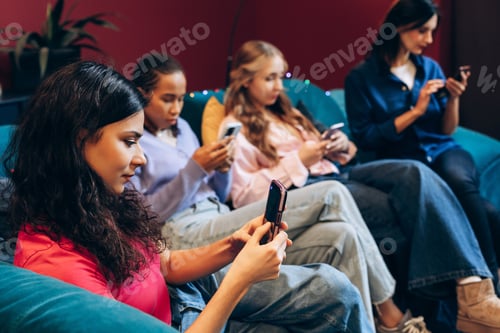 Preview: Group of multinational young women sitting on couch using smartphones