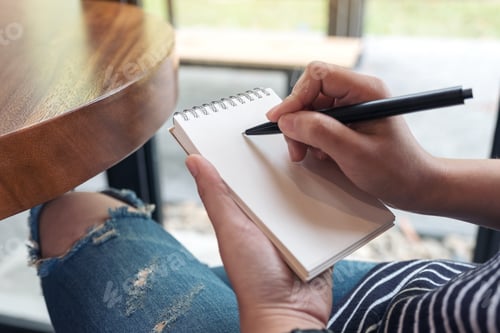 Preview: Closeup image of a woman's hands writing down on a white blank notebook