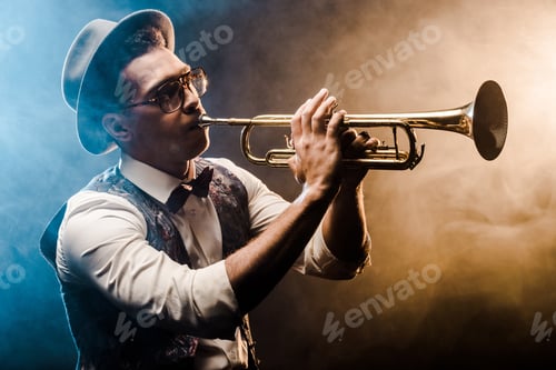Preview: young jazzman playing on trumpet on stage with dramatic lighting and smoke
