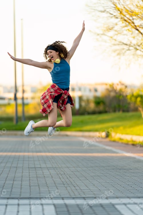 Preview: Joyful young woman leaping with arms wide open in a sunny park.