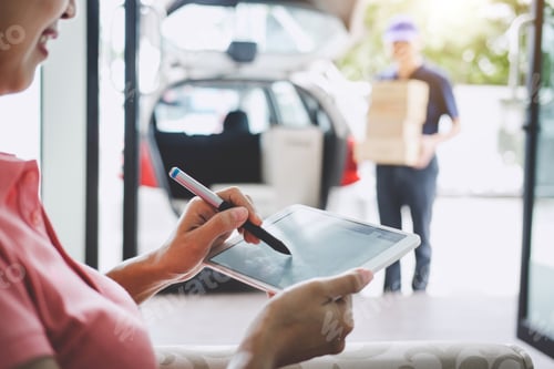 Preview: Woman customer appending signature in digital tablet and receiving a cardboard boxes parcel from