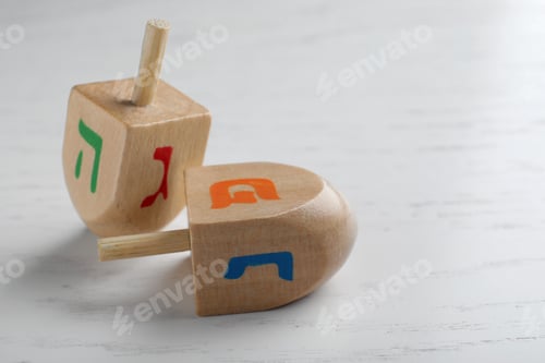 Preview: Hanukkah traditional dreidels with letters Hei, Nun, Gimel and Shin on white wooden table, closeup
