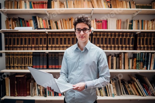 Preview: Young adult caucasian man indoors library holding computer