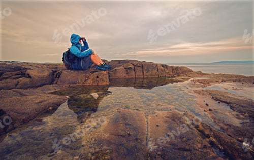 Preview: Man in blue jacket sitting on a rocky coast reflected in water at Barna, Galway, Ireland, adventure