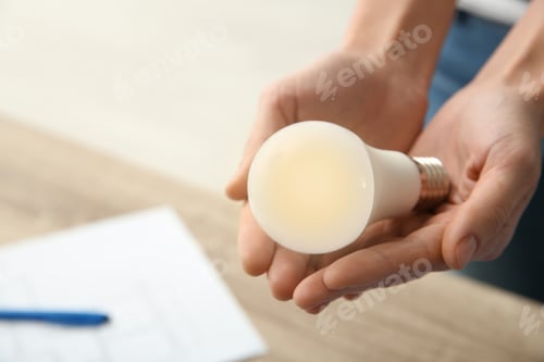 Preview: Woman holding lamp bulb on blurred background, closeup with space for text