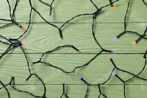 Preview: Black garland with colored lights on green wooden background, top view
