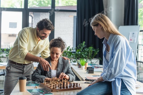 Preview: Smiling businessman pointing with finger at chess near interracial colleagues in office