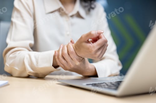 Preview: Woman in office experiences wrist pain while using laptop, highlighting workplace strain and health