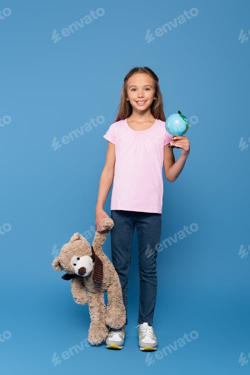 Preview: Smiling child holding soft toy and globe on blue background