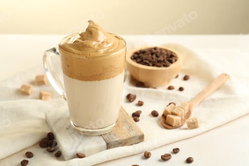 Preview: Delicious dalgona coffee in glass cup, beans and brown sugar on light table, closeup