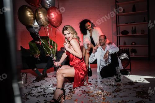 Preview: selective focus of cheerful blonde girl in red dress holding balloons and champagne glass near