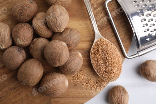 Preview: Spoon with grated nutmeg, seeds and grater on white table, flat lay
