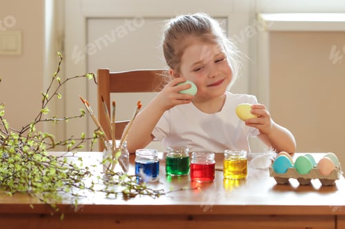 Preview: The girl sits at the table and paints Easter eggs. Preparation for Easter