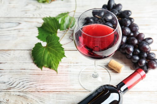 Preview: Glass and bottle of red wine with fresh ripe juicy grapes on table