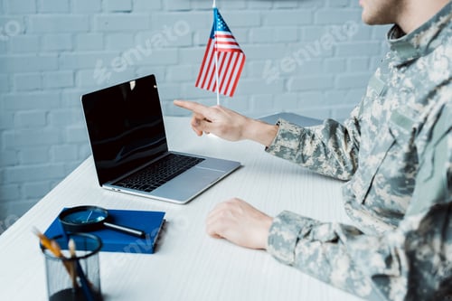 Preview: cropped view of military man pointing with finger at laptop with blank screen