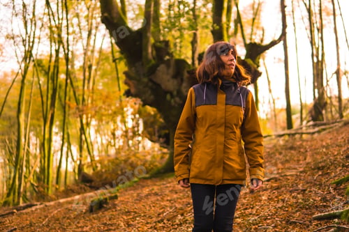 Preview: Lifestyle, a young woman in a yellow jacket walking backwards along a forest