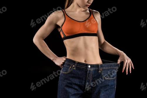 Preview: cropped shot of woman wearing large jeans isolated on black, weight loss concept