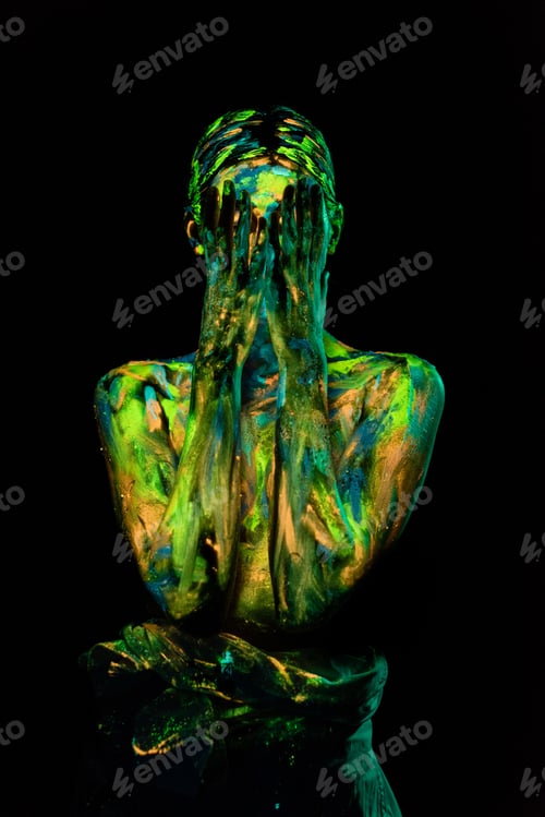 Preview: obscured view of woman painted with ultraviolet paints covering face on black backdrop