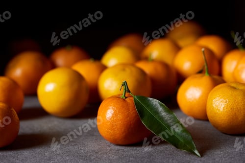 Preview: selective focus of orange clementine with green leaf near tangerines on grey table