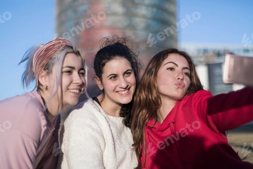Preview: Three happy best girlfriends outdoors making selfie on smartphone.