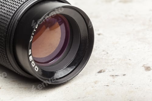 Preview: Close-up view of a black camera lens resting on a textured surface