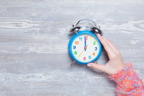 Preview: Female hand holding clock on a table.