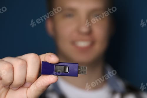 Preview: Man with usb flash drive against blue background, focus on device. Space for text
