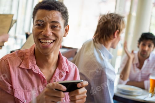 Preview: Urban Lifestyle. Three young men in a cafe. One checking his smart phone. Two talking at a table.