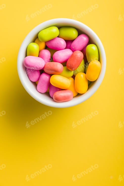 Preview: Colorful hard mint Candies in bowl on yellow background. Top view.