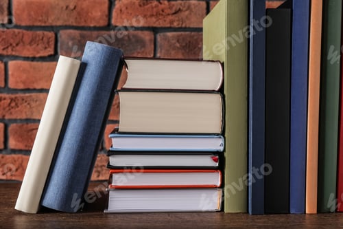 Preview: Many hardcover books on wooden table near brick wall