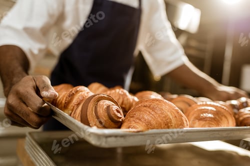 Preview: cropped shot of baker holding tray with croissants on baking manufacture