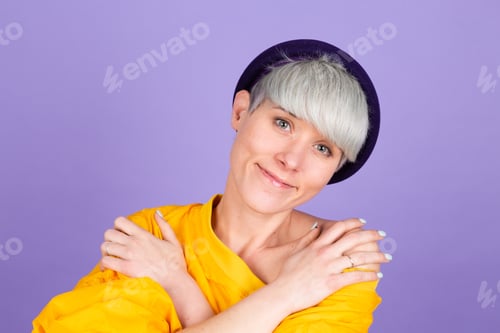 Preview: Stylish european woman on purple background self care hugging herself with smile and closed eyes