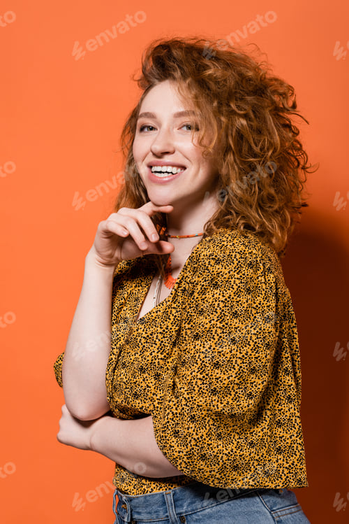 Preview: Happy young red haired woman in necklaces, yellow blouse with abstract pattern