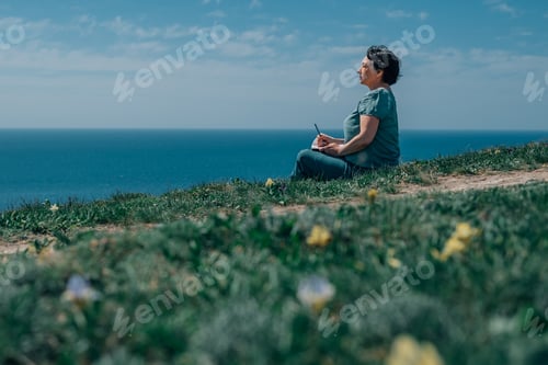 Preview: adult woman writes plans in a diary in the summer on a mountain against the background of sky, sea