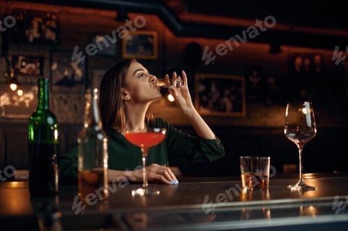 Preview: Stressed woman drinks alcohol at counter in bar