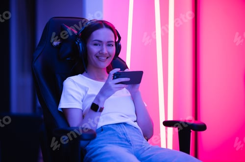 Preview: Beautiful young woman in white shirt with jeans uses smartphone in multicolored neon pink light at