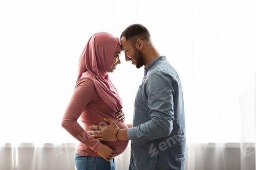 Preview: Pregnant Black Muslim Woman And Her Husband Hugging Near Window At Home