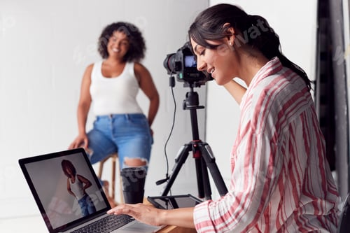 Preview: Female Photographer In Digital Studio Shooting Images On Camera Tethered To Laptop Computer