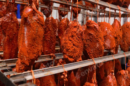 Preview: pieces of pork delicacies in paprika and spices are hung on a metal rack in a meat-packing plant or