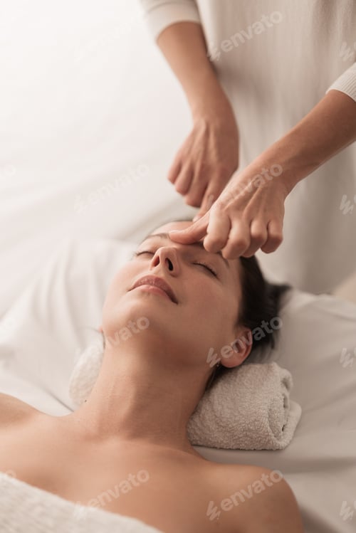Preview: Crop therapist doing facial massage to female customer lying on table in salon
