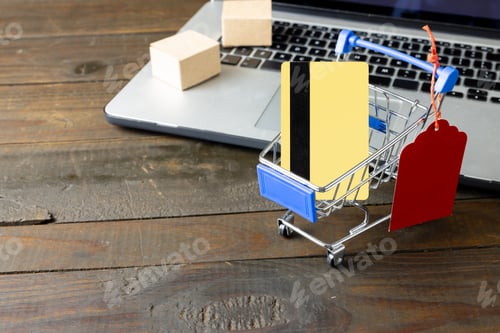 Preview: Composition of shopping cart with credit card and laptop on wooden background